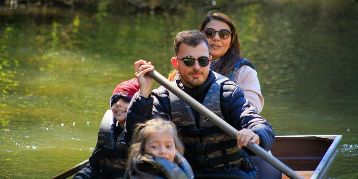 A family of four rowing a canoe on a serene lake during a sunny day, enjoying an outdoor adventure.