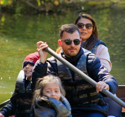 A family of four rowing a canoe on a serene lake during a sunny day, enjoying an outdoor adventure.